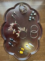 View of a wooden tray displaying a variety of earrings and two bracelets.