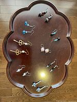 Top-down photo showing eight pairs of various earrings arranged on a wood table with a decorative edge.