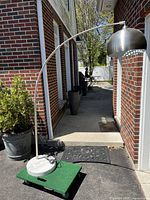 Full lamp showing marble base on dolly, arched metal pole, and dome-shaped metal lampshade.