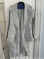 Full view of the handmade women's shimmery suit set including blazer and pants on a hanger against a white door.
