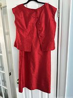 Red handmade silk two piece set hanging on black hanger showing front with sleeveless top and skirt.