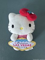 Front view of Hello Kitty plush showing the character holding a 'Welcome to Fabulous Las Vegas Nevada' sign with tags attached.