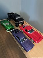 Lot of 4 metal model cars arranged on wooden surface showing different styles and colors.