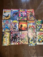 Top view photo of all 15 superhero comic books laid out on a wood floor showing colorful covers featuring characters from DC and Marvel comics.