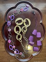 Three necklaces arranged on a wooden tray, each with purple or beige elements.
