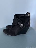 Side profile of a black suede wedge bootie with a decorative buckle strap.