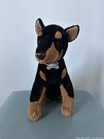 Front-facing view of Rusty the Dog plush showing detailed face, collar with bone-shaped tag, and sitting posture.