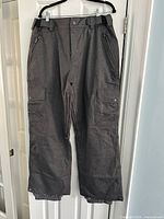 Front view of gray Sessions men's ski pants hung on hanger showing zipper, button, pockets and belt loops.