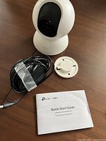TP-Link Tapo C200 camera with power cord, mounting bracket, and quick start guide on wooden surface.