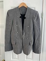 Front view of gray women's blazer hanging on a hanger. Shows double-breasted button front, flap pockets, and scalloped neckline.