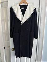 Full view of black vintage dress with white large collar and front buttons hanging on door.