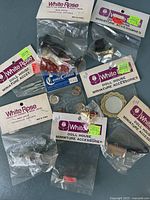 Photo shows multiple small packaged dollhouse miniature accessories from White Rose and Colonial Craftsman brands laid flat on a dark surface.