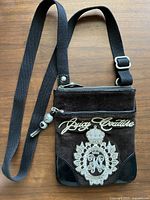Front view of vintage Juicy Couture crossbody bag showing chocolate brown suede, embroidered logo and crest, black leather accents, and black adjustable strap.