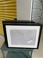 Stacked view of 8 black IKEA Ribba frames from the front showing white mats and plastic covers, approx 16x20 inches.