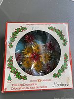 Original boxed Alderbrook tree topper decoration showing the front of the box with window display of the red and yellow starburst lights.