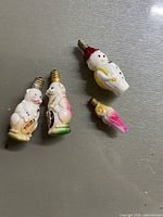 Four antique milk glass Christmas light bulbs including two animals, a bird, and a snowman.