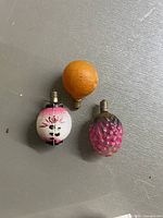Photo showing three antique milk glass Christmas light bulbs in fruit and lantern shapes on a white textured surface.