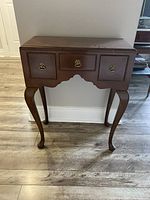 Front view of antique wooden hall table showing three drawers and cabriole legs on wood floor.