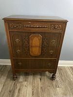 Front view of antique wooden dresser showing detailed carved drawer fronts, wood grain, and hardware.