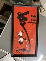 Framed Asian art piece with red background, black calligraphy, and two cranes.