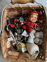 Top view of rectangular wooden basket filled with assorted ornaments including a small doll in red outfit, silver bells, and ceramic pieces.