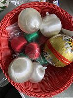 Red basket with white, red, and green silk Christmas balls and a large yellow silk ornament with floral design.