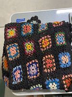 Folded black crochet blanket with multiple colorful crocheted squares attached, showing a variety of colors and patterns in the squares.