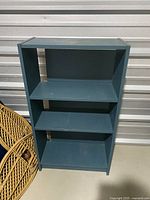 Full view of the blue bookshelf standing in storage unit, showing overall shape and shelves.