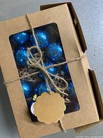 Boxed set of blue mercury glass Christmas bulbs tied with twine, showing reflective shiny blue finish under clear window.