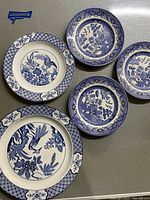 Top-down view of five Blue Willow plates of different patterns and sizes placed on a surface.