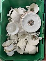 Overhead view of multiple fine china teacups and saucers piled in a green box, showing floral and ribbed design patterns