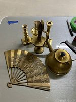 Photo of the full brass lot showing three candlesticks, tea pot, fan, and vase on a table.