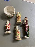 Four ceramic Santa Claus figurines and one decorative ceramic bowl with holly design on tabletop.