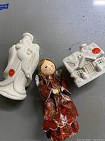 Shows three Christmas decor items: two white ceramic angels and a red fabric angel figurine.