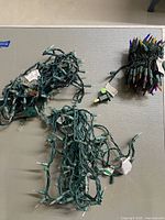 Three tangled bundles of Christmas string lights with green cords; one has multicolored bulbs, two have clear bulbs.