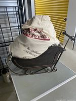 Wooden Christmas sleigh with cream canvas sack displaying festive text, positioned on a table.