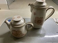 Photo showing both Denby teapots, one tall and one short, set on a table showcasing floral designs and speckled glaze.