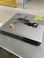 Silver DVD player on table with red, white, and yellow AV cables placed on top.