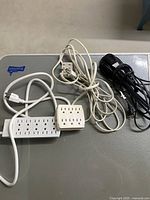 Photo showing four different extension cords and power strips placed on a grey surface, tangled together.
