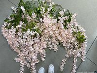 Top-down image showing the full length of the faux wisteria flower garland laid out on the floor, with clusters of light pink flowers and green leaves visible.