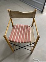 Front view of the wooden folding director's chair showing beige canvas backrest and seat with red and white striped seat cushion.