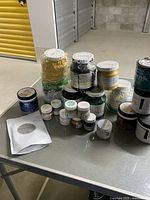 Photo showing an assortment of paint jars and containers on a metal surface, including gold, black, green Fusion paint and others.