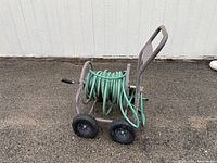 Full view of the metal garden hose reel cart with green hose coiled and four wheels, two of which are deflated.