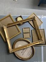 Photo showing seven gilt picture frames of varying shapes and sizes arranged on a tiled floor with some frames stacked.