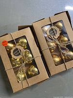 Two gift boxes each containing six gold mercury glass bulbs tied with string.