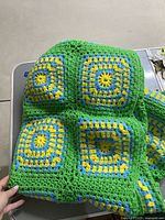 Close-up photo showing four green, yellow, and blue crocheted granny squares joined together in the throw blanket.