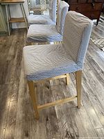 Side view of one IKEA bar-height stool showing removable fabric cover in vertical stripes and wooden legs with footrest.