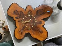 Medium size live edge wooden wall clock clock face showing natural wood grain with gold numerals and hands.
