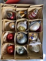 Top-down photo of 12 assorted vintage mercury glass bulb ornaments packed in cardboard box with dividers and tissue paper.