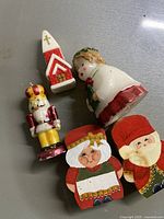 Christmas figurines including wax nutcracker, angel, church, and wooden Santa and Mrs Claus faces on gray surface.